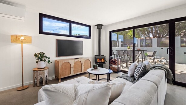 Un salon moderne avec un canapé, un téléviseur, une cheminée et un balcon aménagé avec du mobilier d’extérieur.
