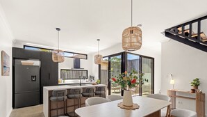 Une cuisine moderne dotée d’un îlot central, d’un coin repas avec une table et des chaises, et d’un escalier menant à un niveau supérieur.