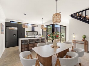 A modern kitchen with a central island, dining area with a table and chairs, and a staircase leading to an upper level. - Stone River Villa 2 | Private Escape | Heated Pool (Margaret River)