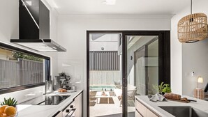 Une cuisine moderne dotée d’une grande fenêtre, d’un four encastré et d’un coin repas visible à travers une porte ouverte.