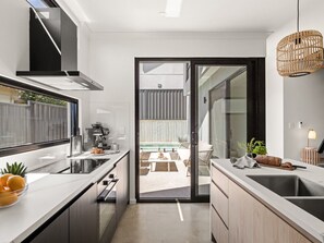 A modern kitchen with a large window, a built-in oven, and a dining area visible through an open door. - Stone River Villa 2 | Private Escape | Heated Pool (Margaret River)