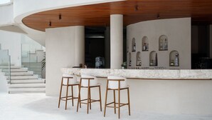 A modern bar area with a curved counter, three bar stools, and a staircase leading to an upper level. - VANARA Resort & Spa (Pecatu)