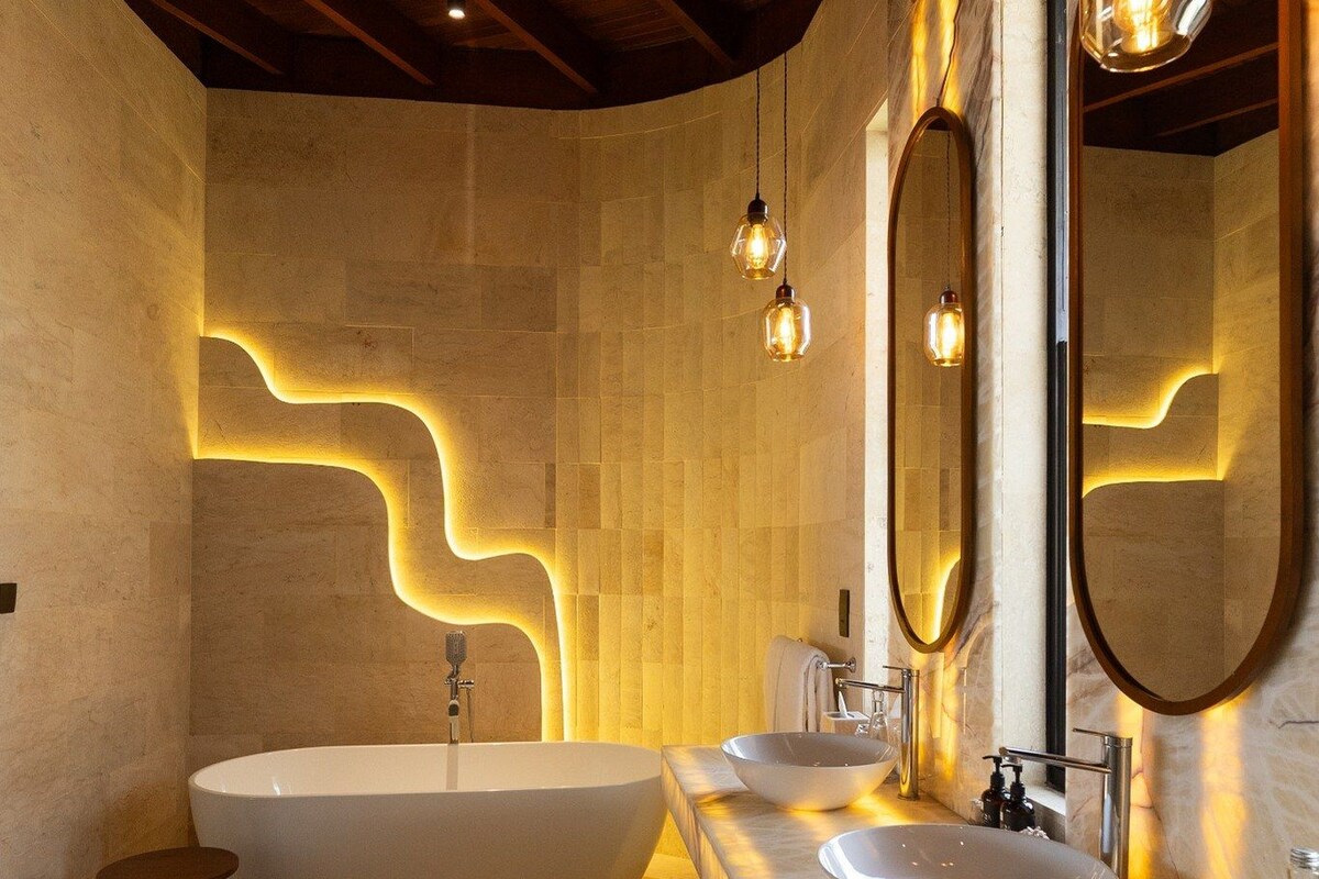 A modern bathroom with a freestanding bathtub, two sinks, and decorative lighting.