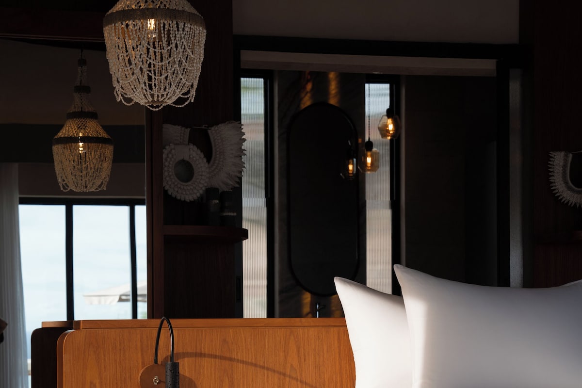 A modern bedroom with a wooden headboard, a large bed, a built-in toilet, and a large window with a view.
