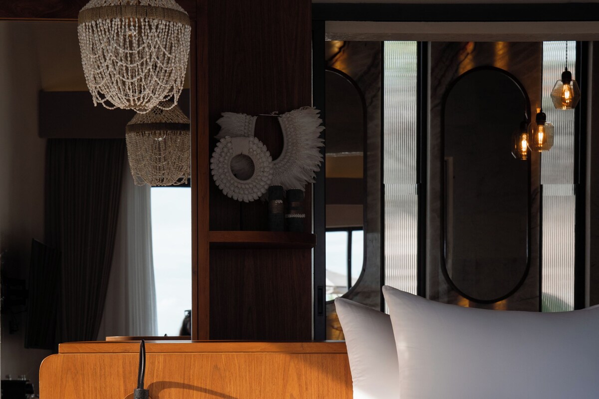 A modern bedroom with a wooden bedside table, a built-in toilet, a large bed, and a hanging light fixture.