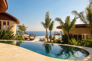 A pool area with a clear view of the ocean, surrounded by palm trees and lounge chairs.