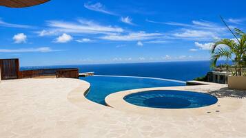 Una piscina infinita con vista al océano, una terraza de madera y una palmera.