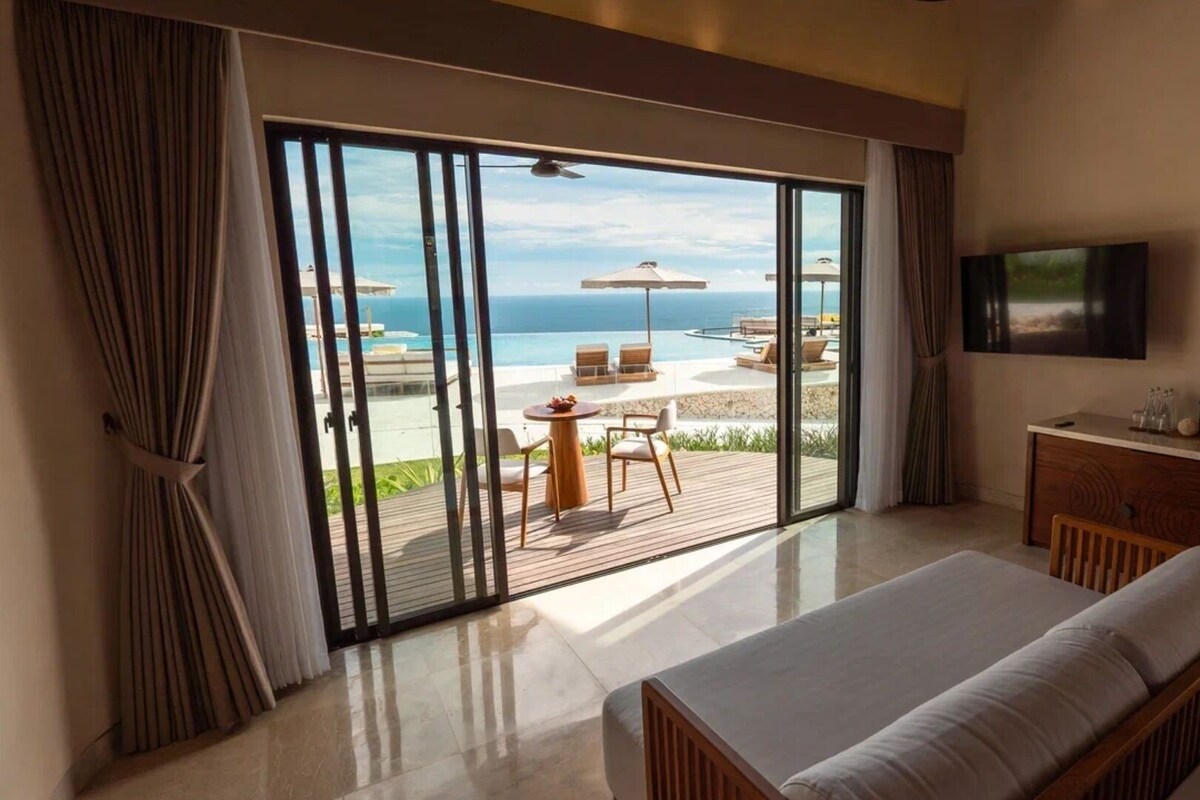 Un dormitorio con un amplio ventanal corredera que da a un balcón con piscina y sillas de playa.