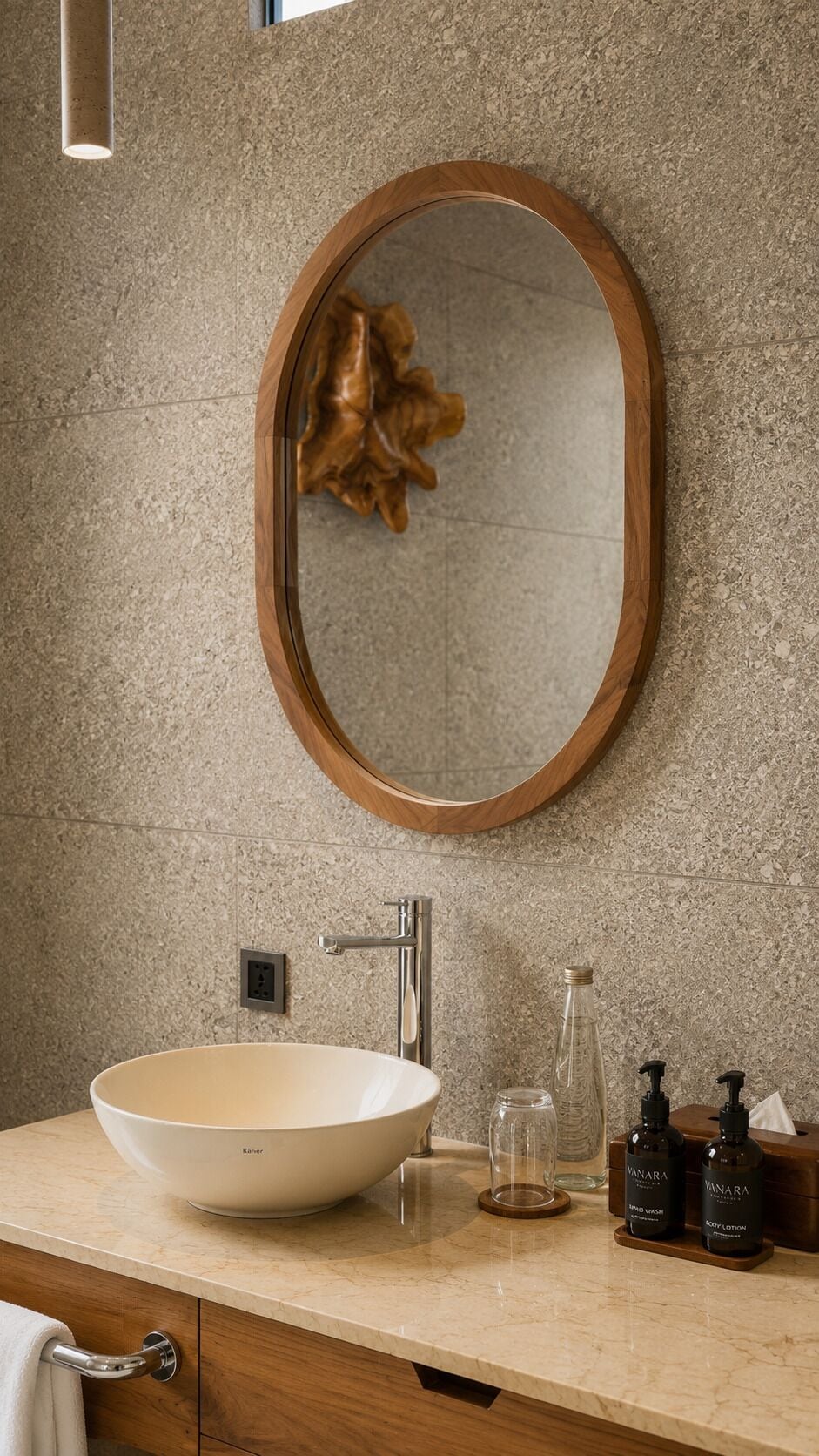 Ein Badezimmer mit einem großen, ovalen Spiegel, einem weißen Waschbecken, einem Wasserhahn und Pflegeprodukten auf der Ablagefläche.