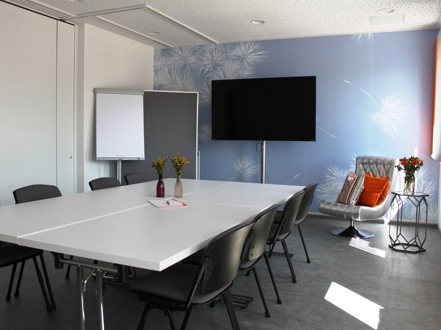 Una sala de conferencias con una larga mesa, sillas, una pizarra, un televisor y jarrones decorativos.