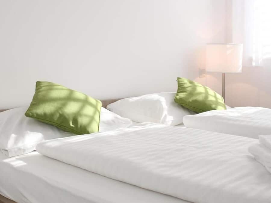 A bed with white bedding and green pillows, a bedside lamp, and a window with curtains.