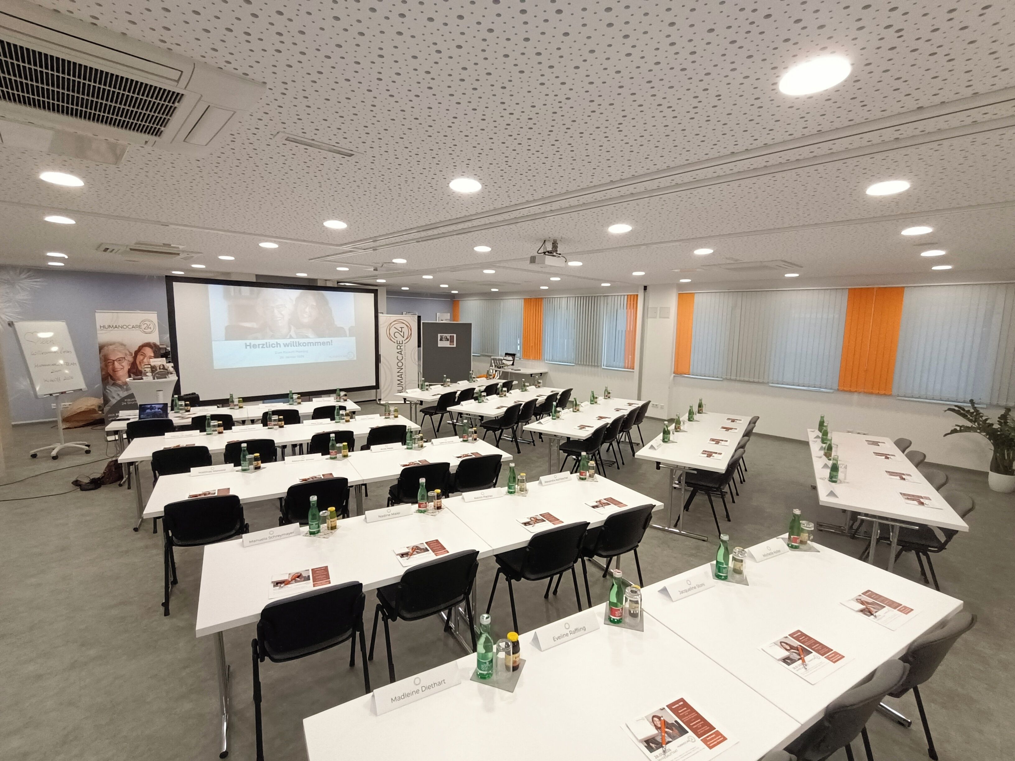 A conference room with multiple tables, chairs, and a presentation screen.