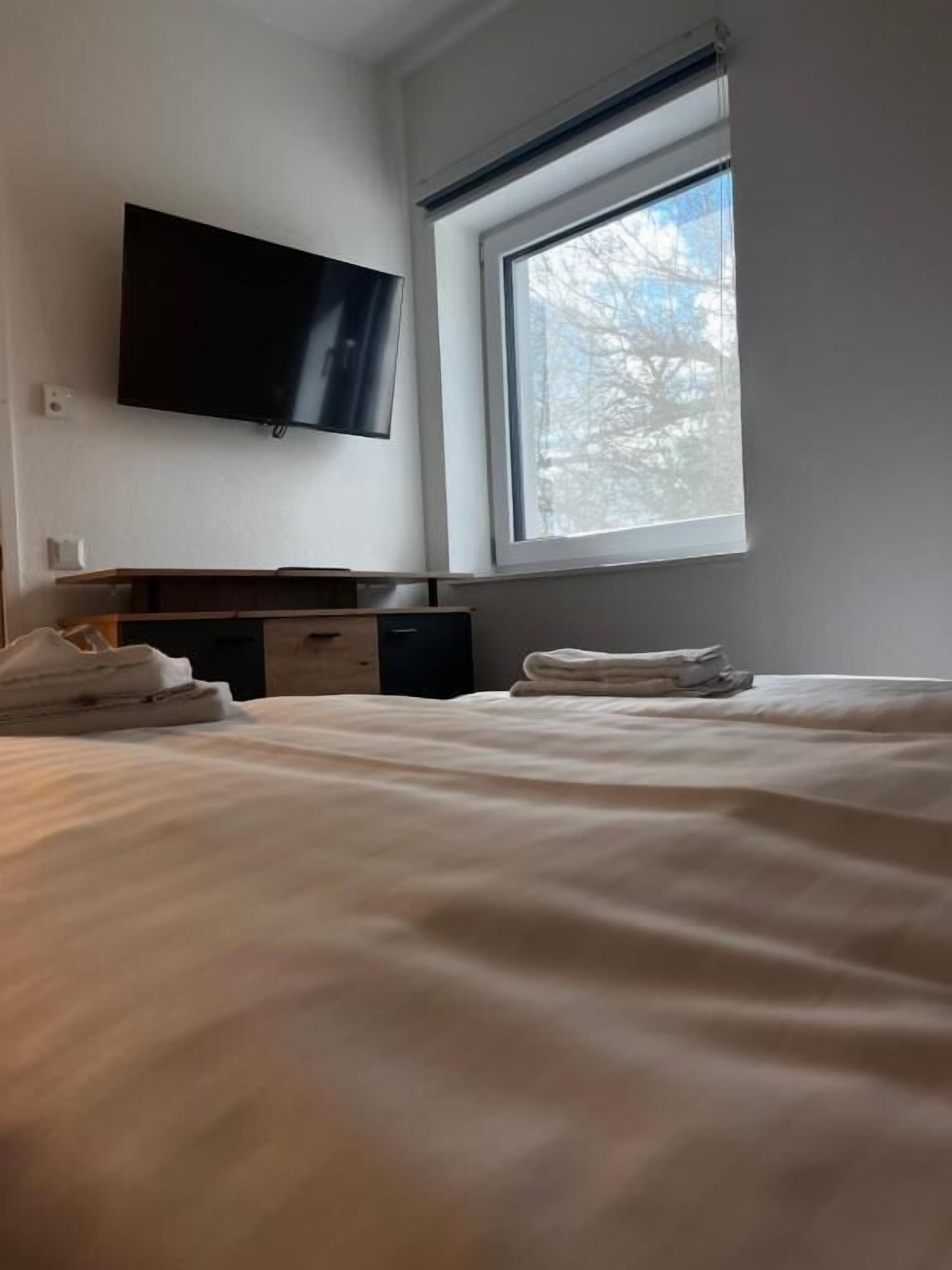 Una habitación de hotel con una cama, un televisor de pantalla plana en la pared, una ventana con vistas a árboles y un aparador de madera.