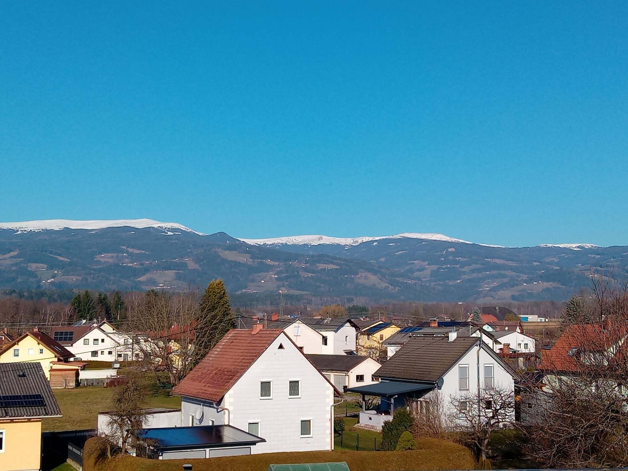 A residential area with houses, a clear sky, and snow-capped mountains in the background.