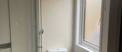 A small bathroom with a toilet, a glass shower enclosure, a window with blinds, and a towel rack.