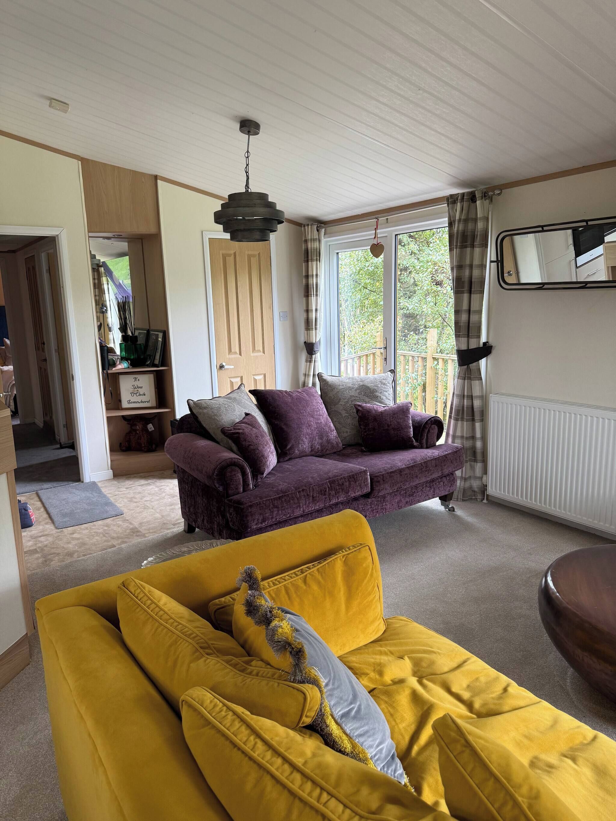 A cozy living room with a purple sofa, a yellow sofa, and a hanging light fixture.