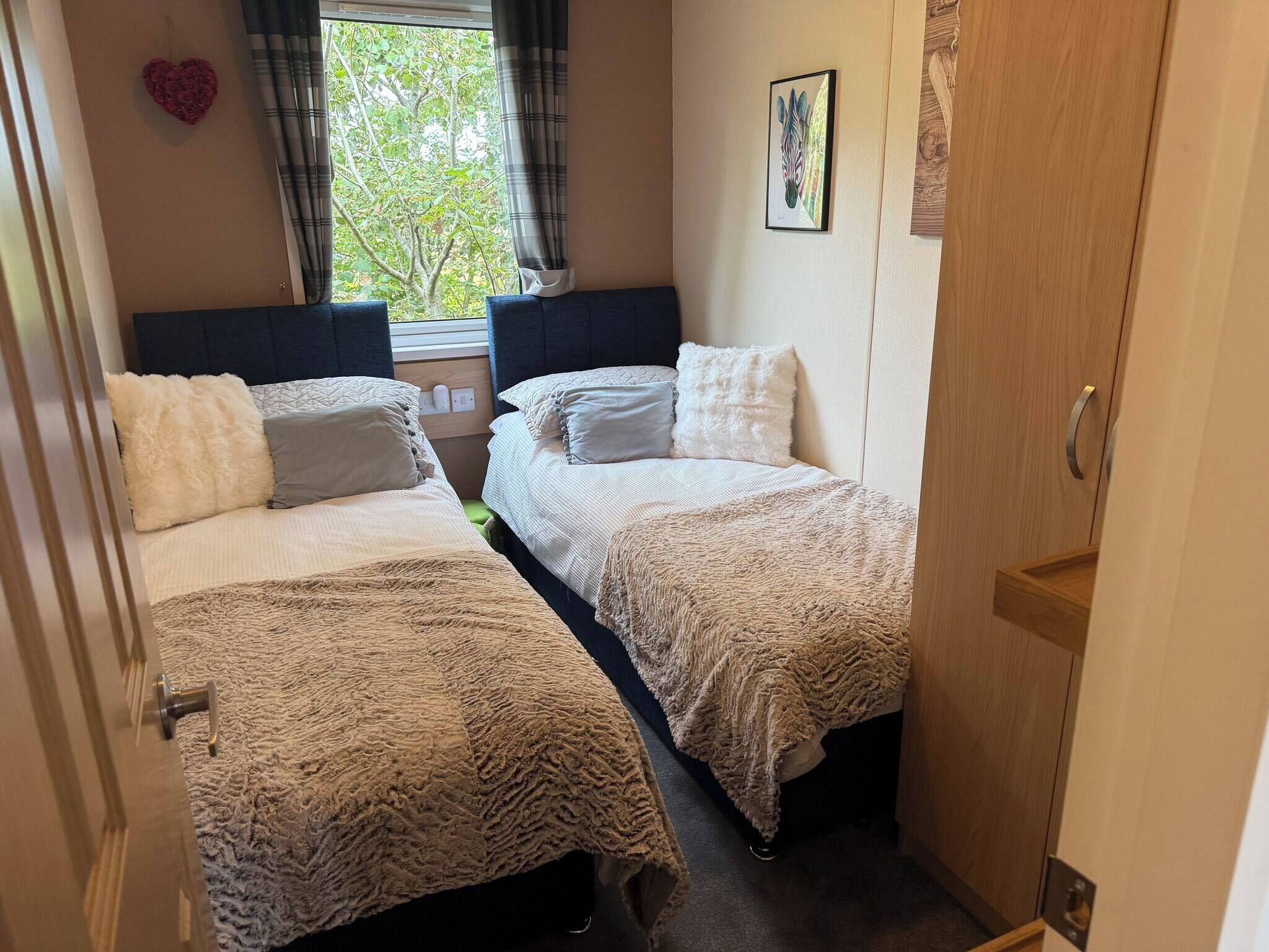 A bedroom with two beds, a window with curtains, a heart decoration, and a zebra painting.