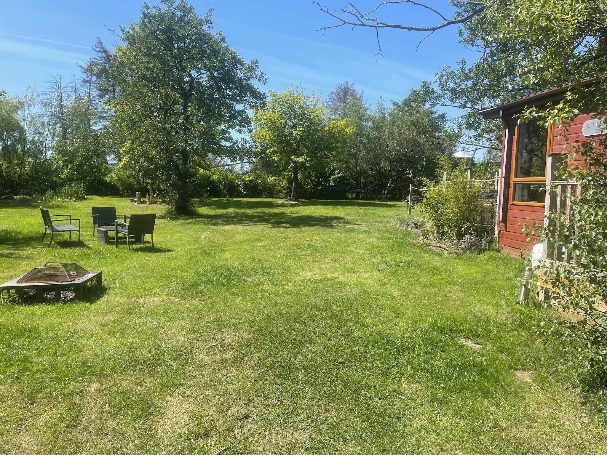 A grassy backyard with a wooden structure, a metal grill, and two chairs.