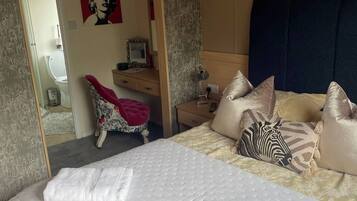 Een slaapkamer met een bed, kussens, een nachtkastje, een spiegel en een deur naar een badkamer.