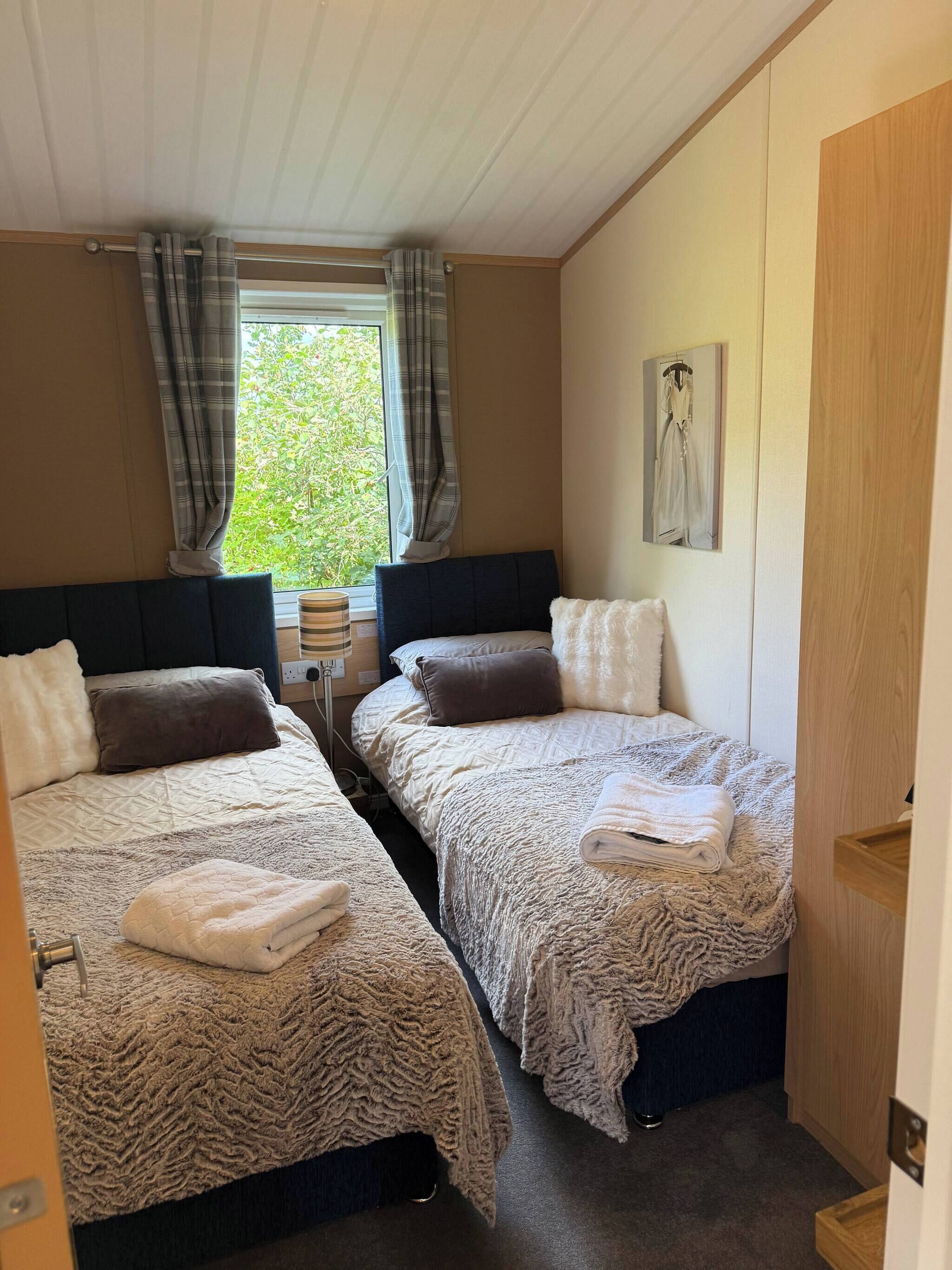 Un dormitorio con dos camas, una ventana con cortinas, una lámpara de noche y un cuadro en la pared.