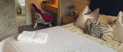 Ein Schlafzimmer mit Bett, Kissen, einem Nachttisch, einem Spiegel und einer Tür zu einem Badezimmer.
