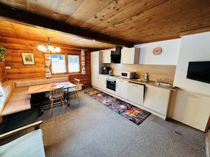 Cocina compacta con comedor, paredes de madera, ventilador de techo y un reloj en la pared.