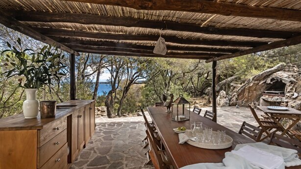 Un'area pranzo all'aperto con tavolo e sedie in legno, pavimento in pietra e vista sul mare.