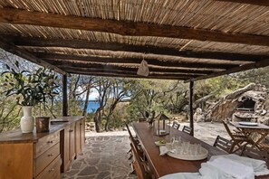 Un área de comedor al aire libre con una mesa y sillas de madera, piso de piedra y vista al mar.