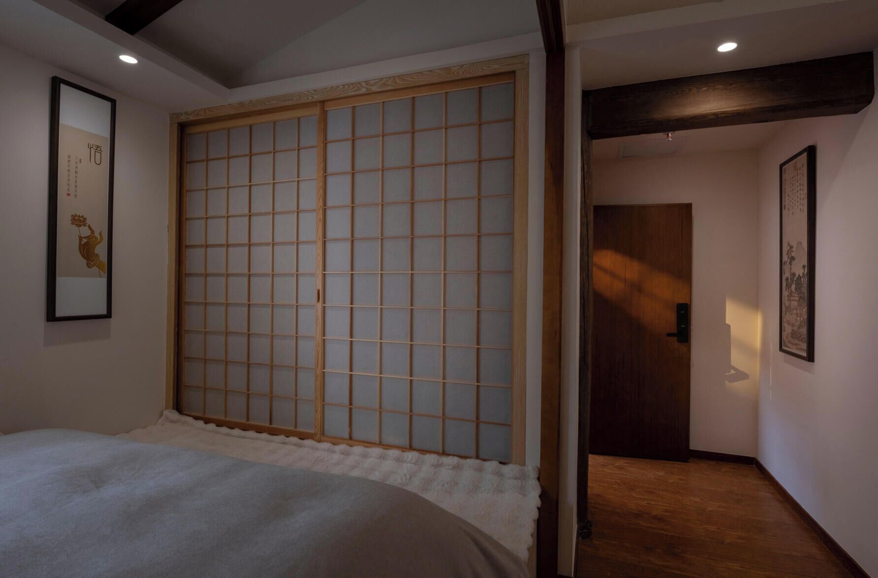 A room with a bed, a sliding shoji screen door, a framed picture on the wall, and a door leading to another room.