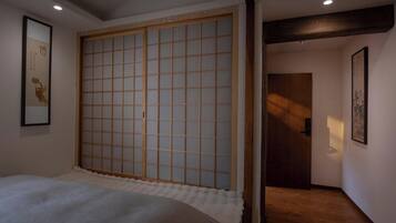 A room with a bed, a sliding shoji screen door, a framed picture on the wall, and a door leading to another room.