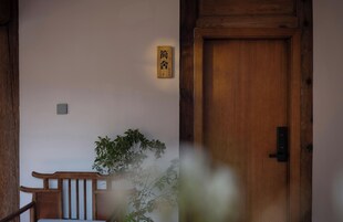 Una puerta de madera con un letrero tradicional japonés, un banco de madera y una planta en maceta.