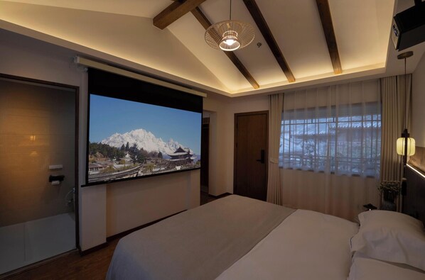 A hotel room with a large bed, a television displaying a scenic view, a wooden ceiling, and a window with curtains. - The Ripplewood Sanctum (Lijiang)