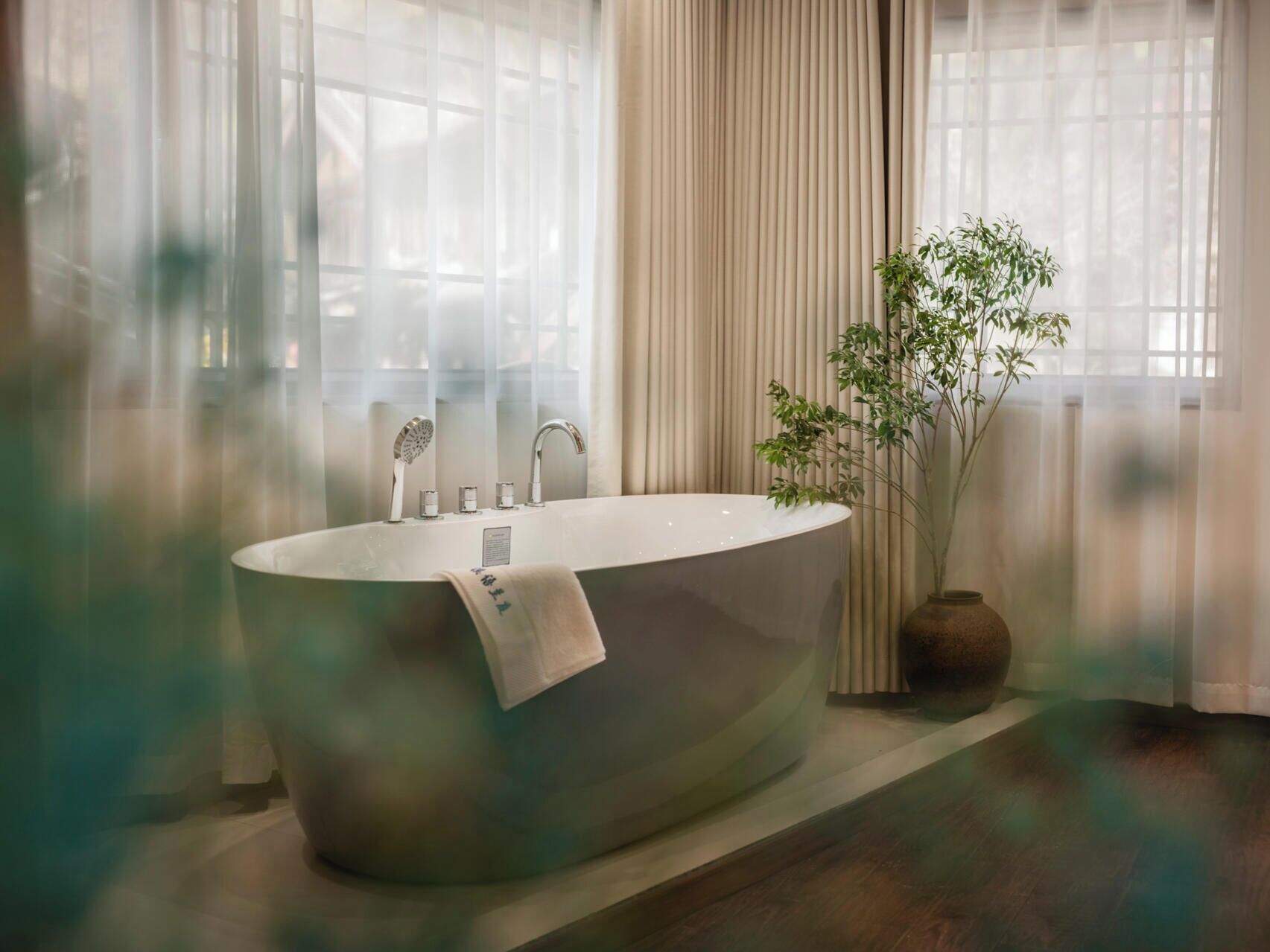Ein modernes Badezimmer mit einer freistehenden Badewanne, einem Spiegel, einem Handtuch und einer Topfpflanze.