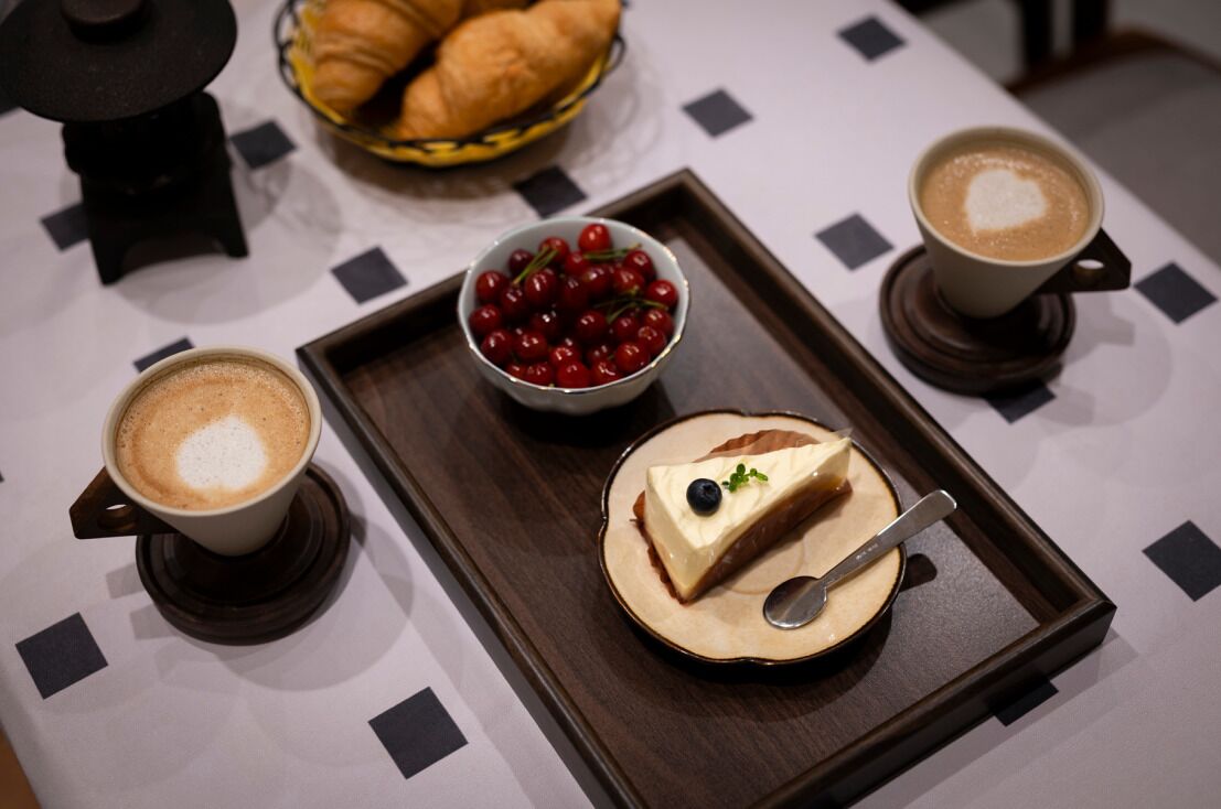 Ein Tablett mit Dessert, einer Schale Kirschen und zwei Tassen Kaffee auf einem Tisch mit geometrischem Muster.