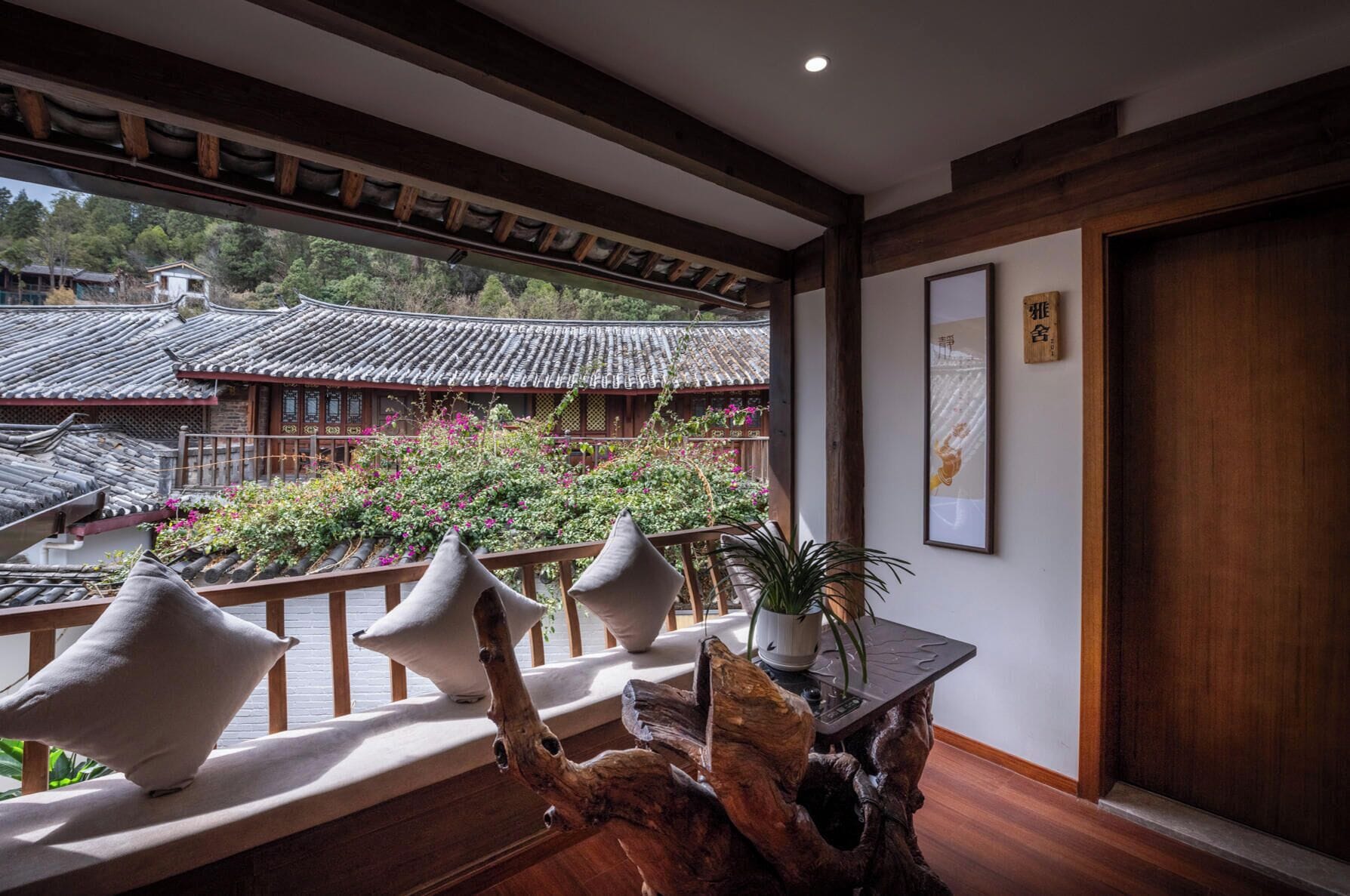 Ett traditionellt japanskt rum med tatamimattor på golvet, ett träbord med en krukväxt och utsikt över en traditionell byggnad med ett tak täckt av tegelpannor.