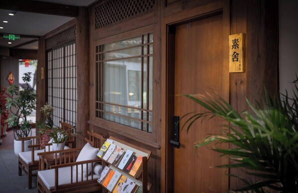 A traditional wooden building with a large window, a wooden door with a sign, and a seating area with books. - The Ripplewood Sanctum (Lijiang)