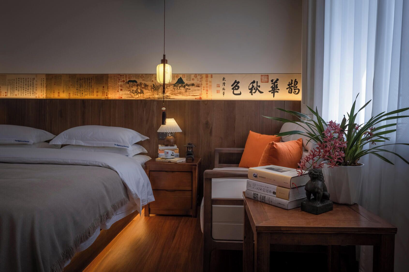 A neatly arranged hotel room with a bed, bedside table, lamp, and a decorative wall with calligraphy.
