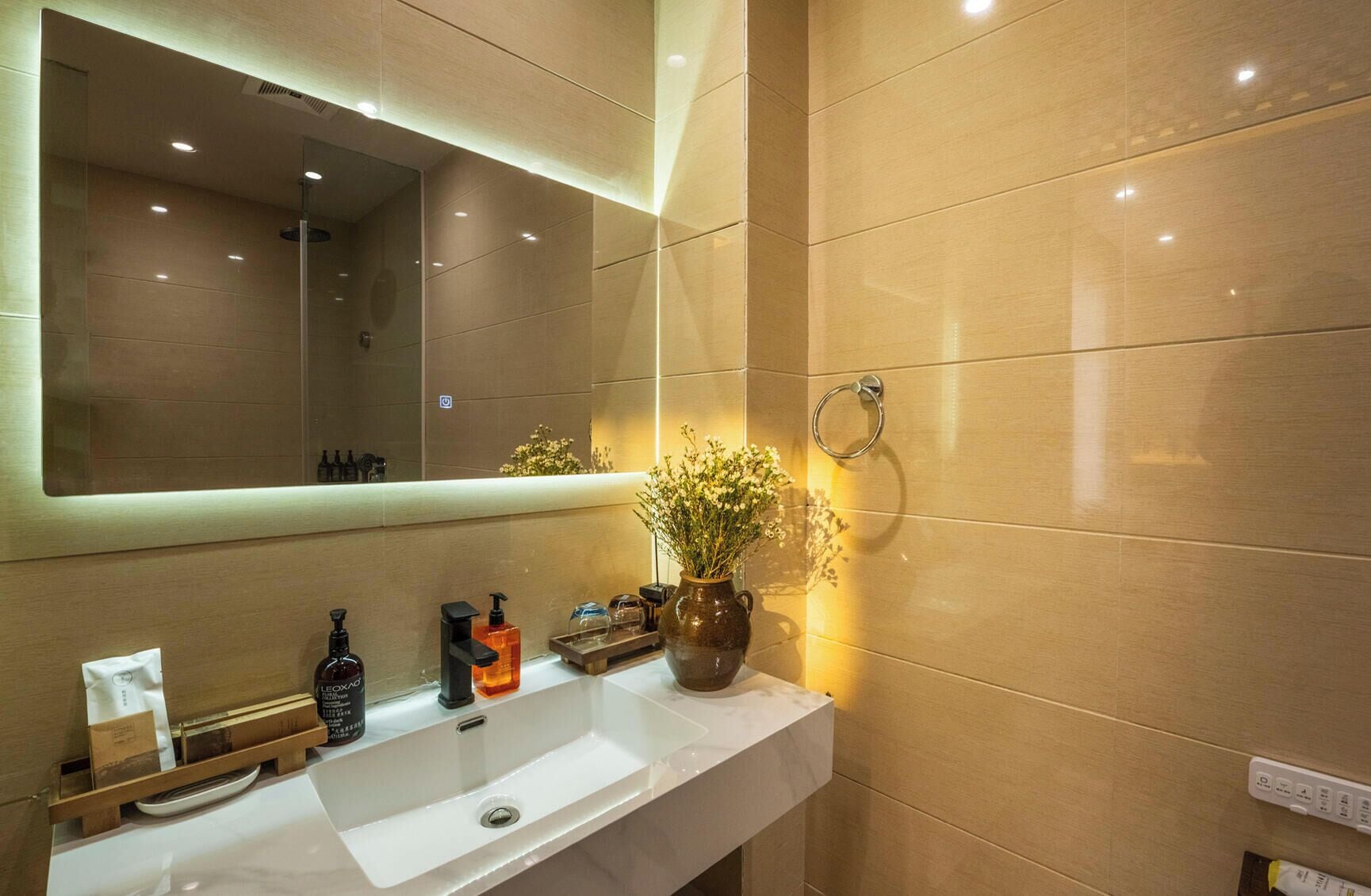 Un baño moderno con un espejo grande, un lavamanos blanco y un florero con flores.