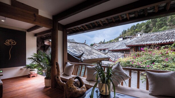 Una habitación con suelo de madera, un ventanal con vistas a edificios tradicionales y un balcón con vista a los edificios y la vegetación.