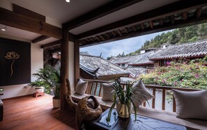 A room with a wooden floor, a large window overlooking traditional buildings, and a balcony with a view of the buildings and greenery. - The Ripplewood Sanctum (Lijiang)