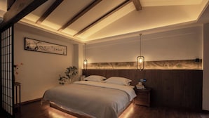 Un dormitorio con una cama grande, vigas de madera, una mesita de noche y una lámpara fijada a la pared.