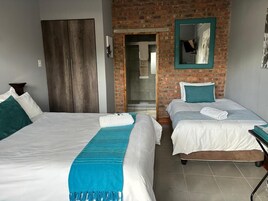 Habitación de hotel con dos camas, una pared de ladrillo, un espejo y una puerta que da a un baño.