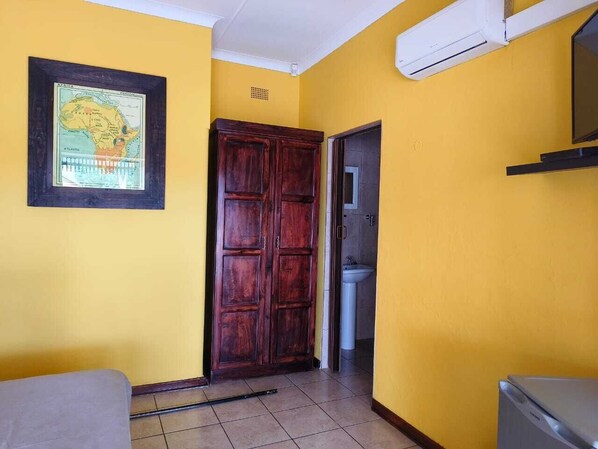 A room with yellow walls, a wooden door, a framed map, a white sink, and a tiled floor. - Spring Day BB (Mkhondo)