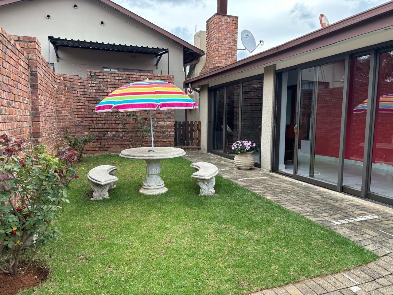 A patio with a round table, two stone benches, and a colorful umbrella.