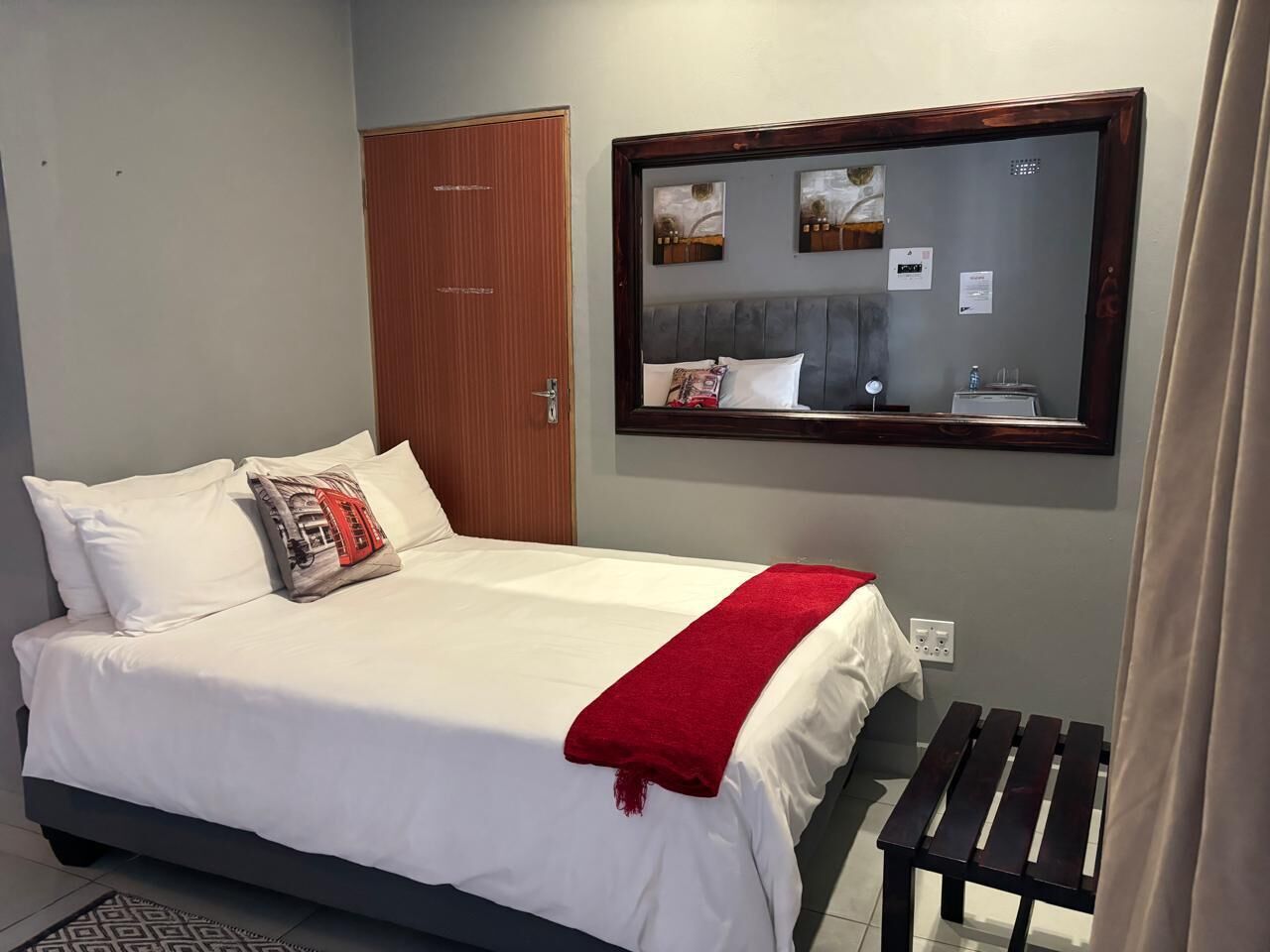 Un lit bien fait, avec des draps blancs, un plaid rouge et un oreiller à motifs rouges et blancs.