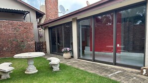 A patio with a round table and benches, a brick wall, and a glass door leading to a red interior.