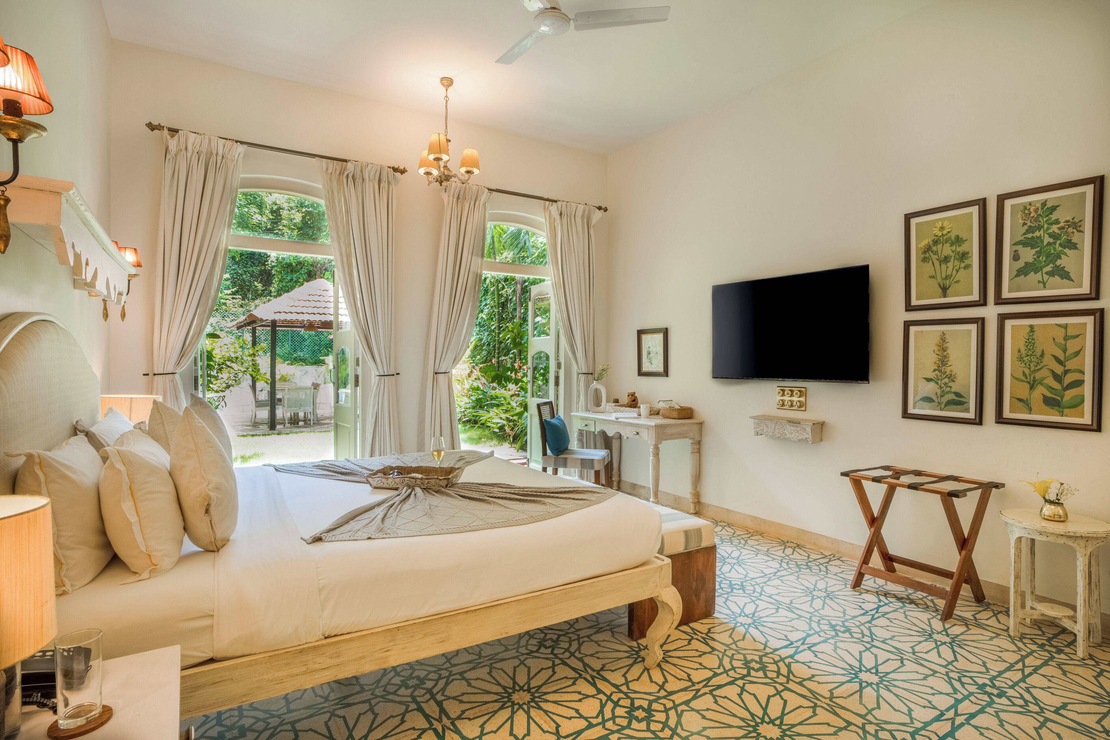 A bedroom with a bed, a desk, a chair, a TV, and a window with curtains.
