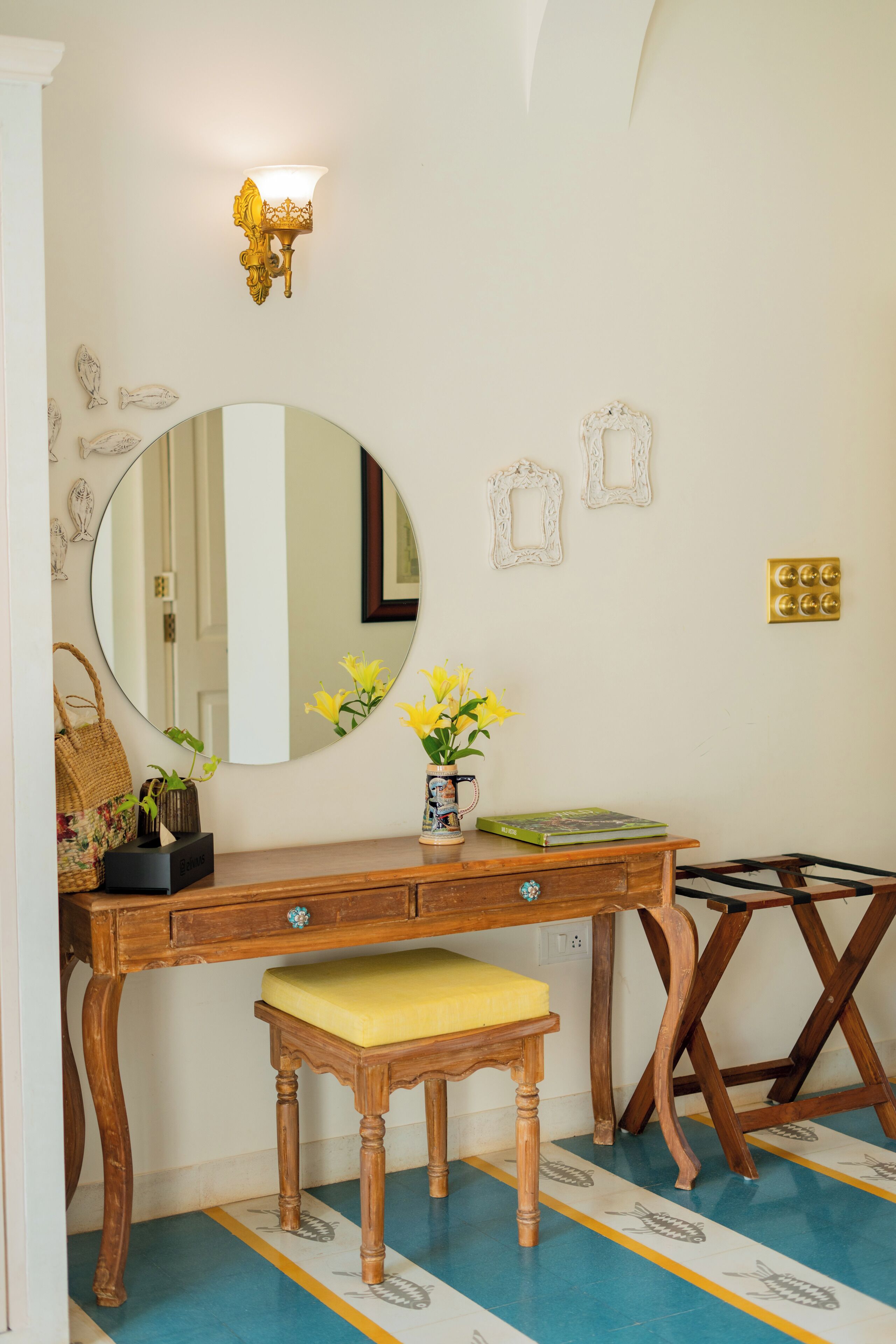 Een kamer met een houten bureau, een ronde spiegel, een gele bank en een wandlamp.