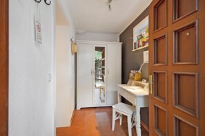 Un pasillo estrecho con una puerta blanca, un escritorio blanco con una silla, y una puerta de madera a la derecha.
