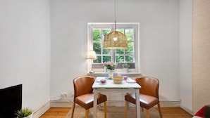 Un coin repas comprenant une table, des chaises, un luminaire suspendu, une fenêtre donnant sur un paysage et un téléviseur placé à gauche.